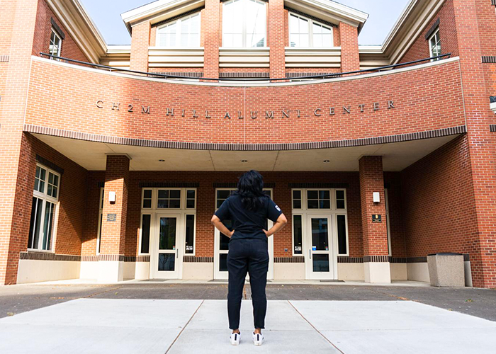 Photo of student standing in front of the alumni center and looking up at the building name