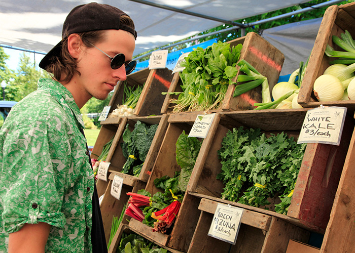 person with green shirt, black ball cap and sunglasses shopping for vegetables at the Corvallis Farmers Market