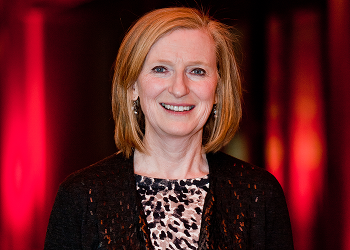 Ruth Beyer dressed for award event and smiling at the camera with dark red curtain background