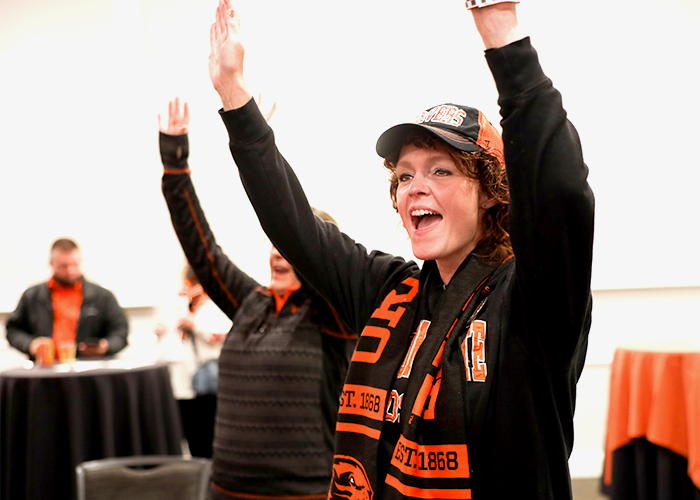Close-up of a Beaver fan in orange and black cheering with hands up while listening to the OSUMB inside the CH2M HILL Alumni Center ballroom