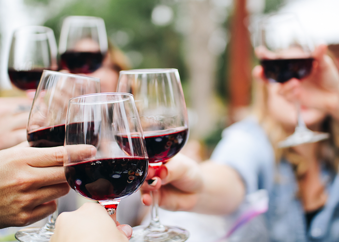 Photo of several hands clinking red wine glases together