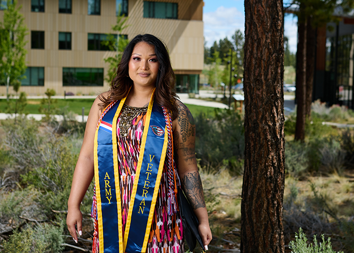 Adrianna smiling at camera while standing outside under Ponderosa Pine on OSU-Cascades OSU's Bend campus