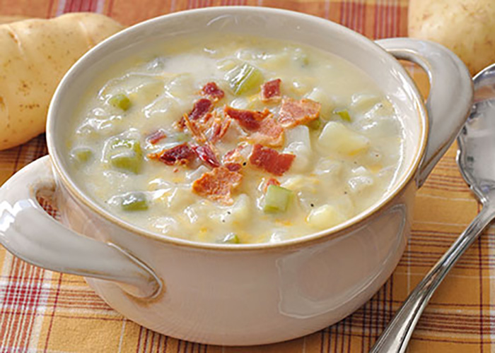 potato soup in a cream colored bowl on a plaid tablecloth covered table