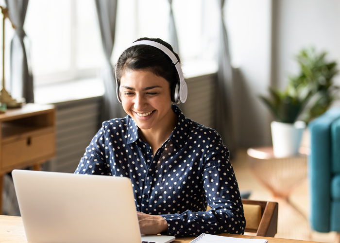 Photo of woman wearing headphones and smiling while using laptop at desk