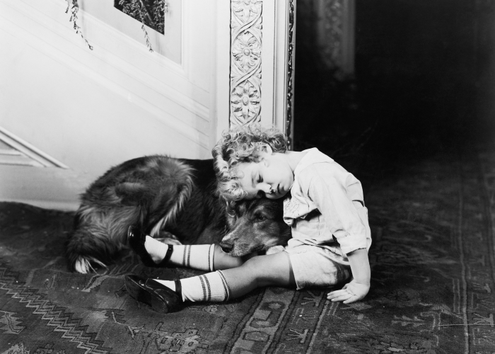 Black and white photo of a child sitting on the floor and leaning on a golden retriever