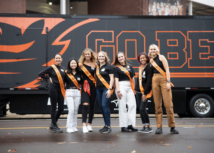 2021 Homecoming Court wearing orange sashes and posing in front of the large Go Beavs semi