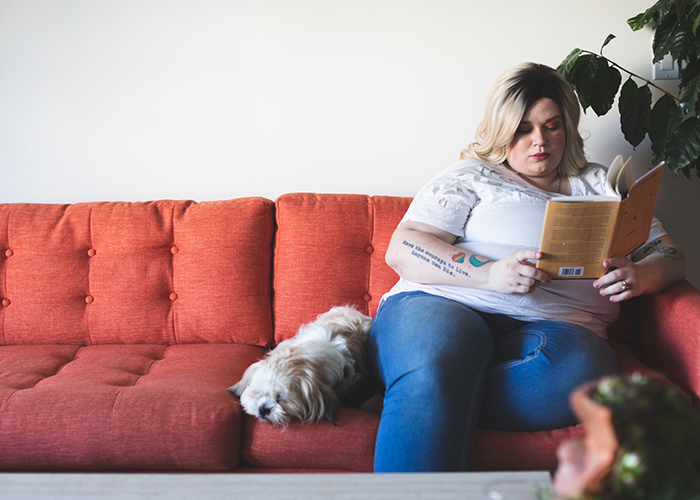 Photo of a woman reading on the couch with her dog