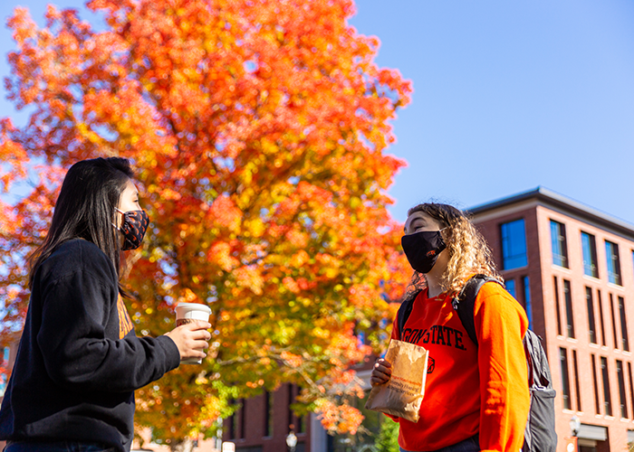 Photo of two students holding coffees and talking while outside on campus in fall 