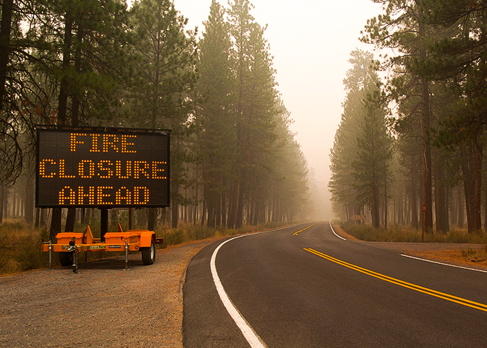 Photo of road without traffic with sign that reads "fire closure ahead" and smoke in th air
