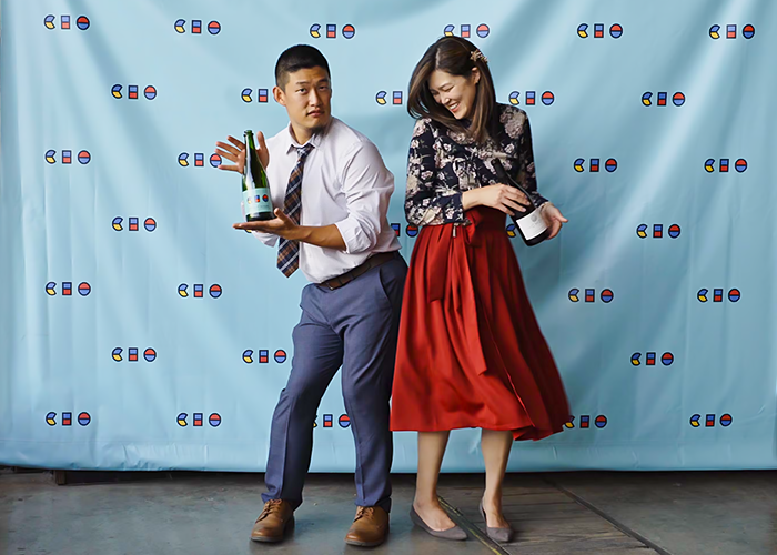 The Chos modeling their product in a fun pose like looks like dancing while in front of a branded draped background