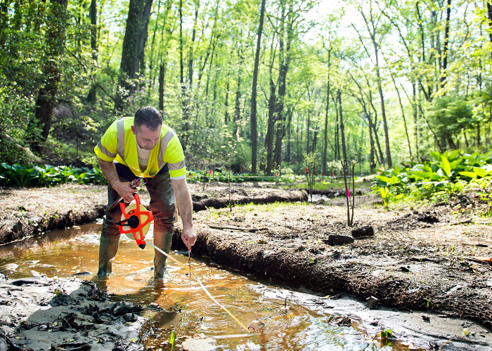 OSU student measuring near while standing in a muddy stream in a forest